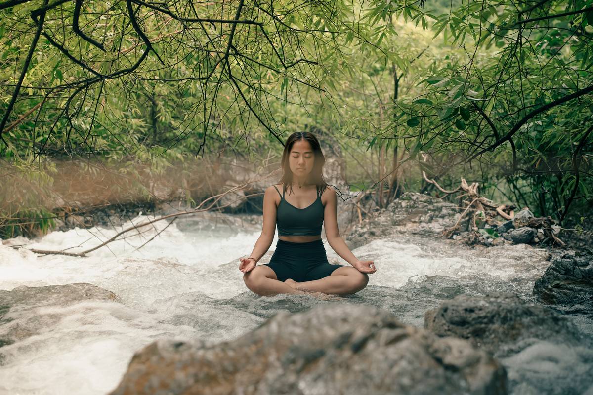 A person sitting cross-legged on a yoga mat near a lake, deep in meditation