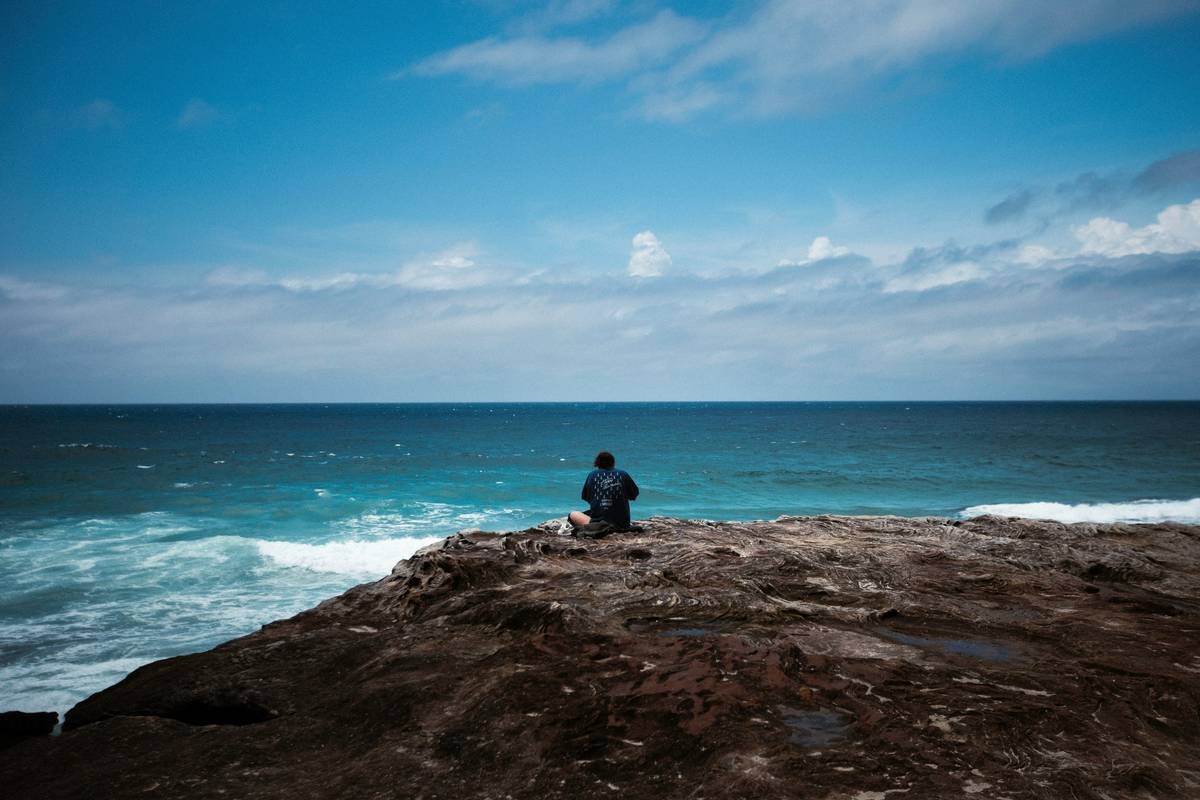 A man sitting on top of a rock next to the ocean