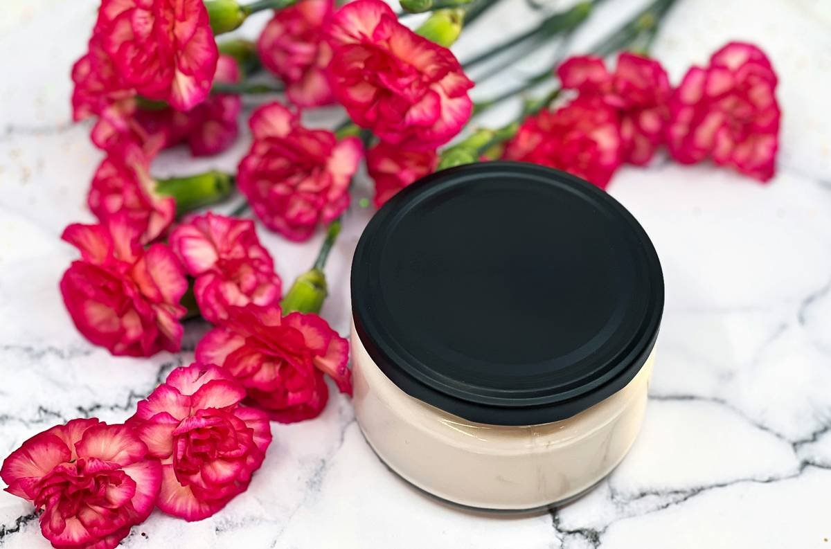Cosmetic cream jar with black lid styled with pink flowers on a marble background, suitable for skincare branding, natural cosmetics, and packaging mockups.