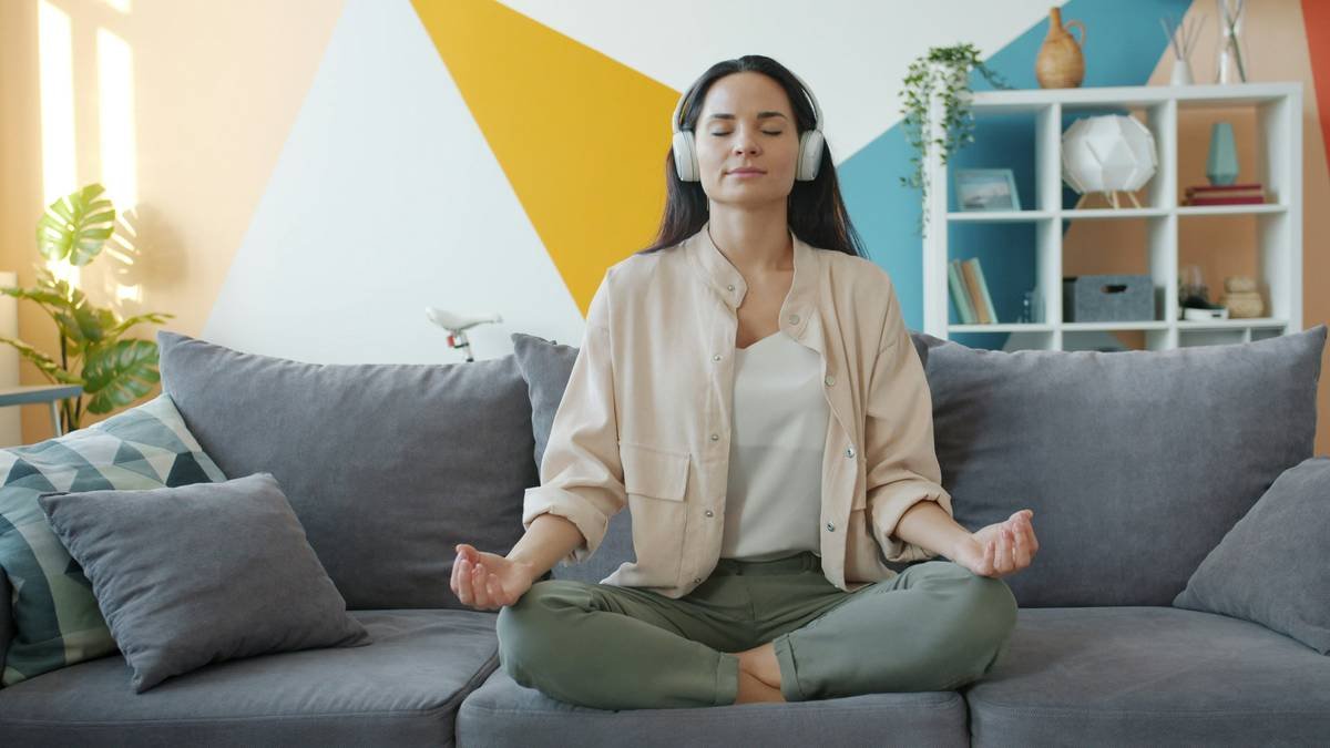 happy girl in headphones listening to music and relaxing lotus position sitting on sofa in apartment enjoying leisure time and modern technology.