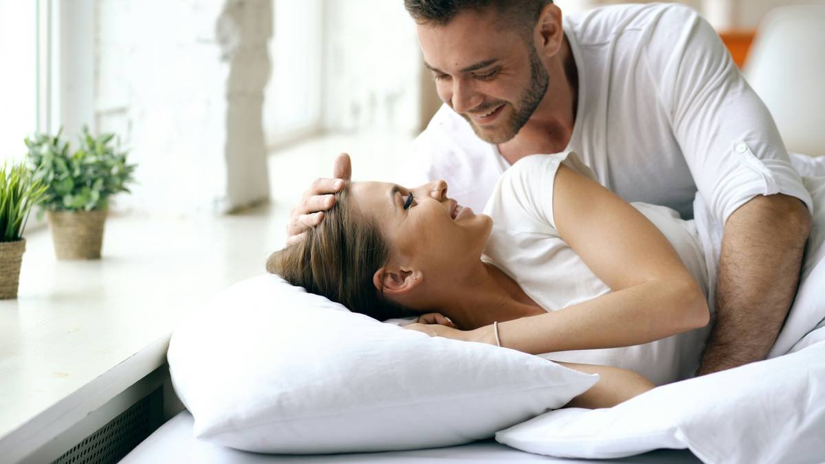 Young beautiful and loving couple wake up at morning. Attractive man kiss and hug his wife in bed